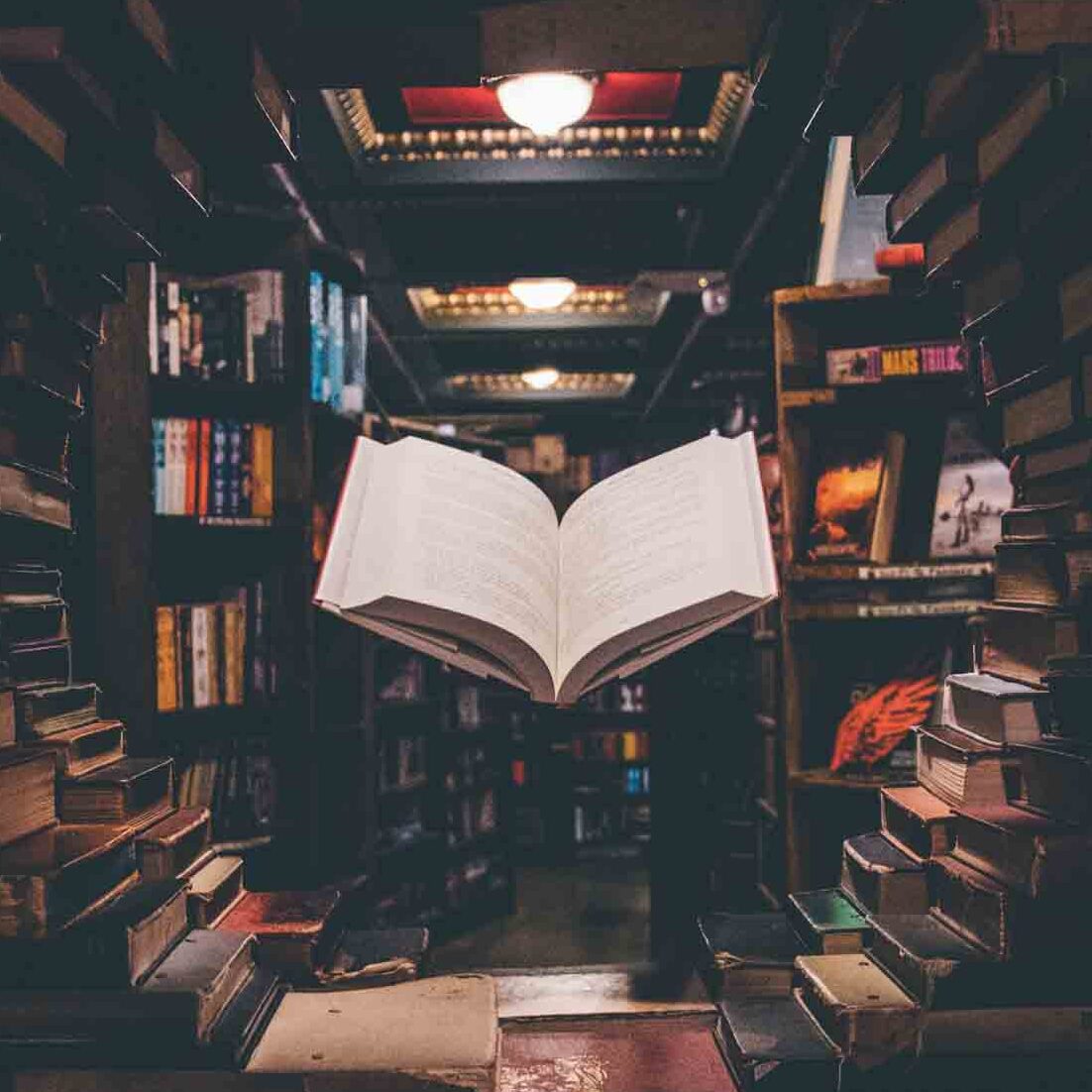 An open book floats above a desk amid stacks of books